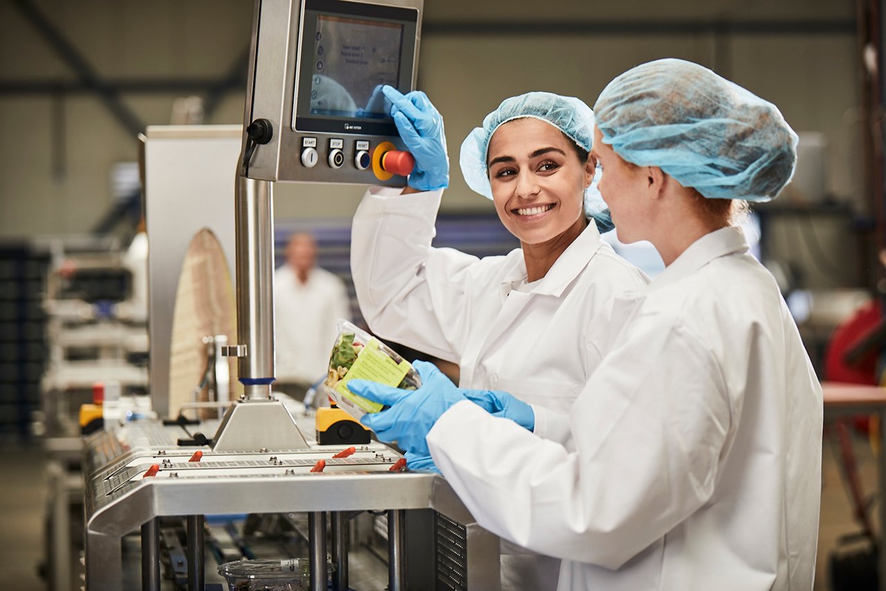 Bedienerinnen an einer Verpackungslinie mit Sleevesystem für Fleisch- und Fischschalen